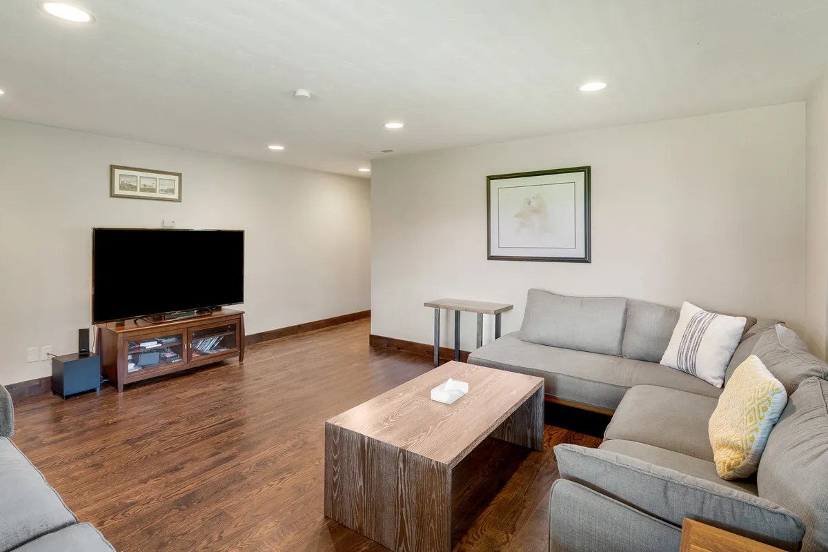 This image depicts a comfortable downstairs living area with plush sofas, a wooden coffee table, a TV stand with a television, and tasteful framed artwork on the walls. The arrangement invites relaxation and togetherness, supporting activities like watching movies or casual gatherings.