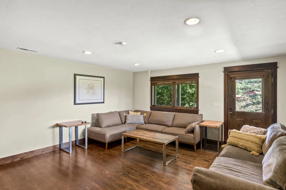 A light-filled sitting area with inviting sofas arranged around a coffee table, near a window and door that allow plenty of natural light. The setting is casual and flexible, ideal for reading, socializing, or enjoying a quiet moment away from the main activity hubs.