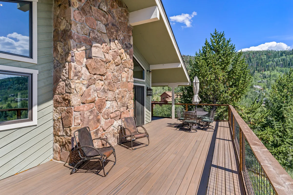 A cozy outdoor deck bordered by a stone wall, featuring comfortable chairs and an outdoor dining table. The deck overlooks a serene treeline, suggesting a peaceful spot for family gatherings, stargazing, or enjoying a meal after active days in nature.