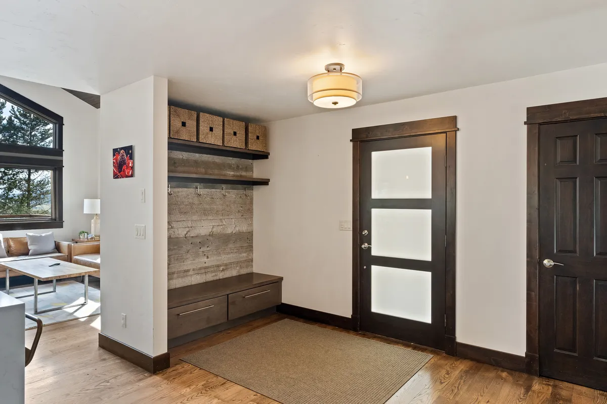 This image captures the entry area of the duplex, featuring the front door, a coat rack, a bench, and storage boxes. The space is functional and inviting, suggesting a welcoming transition from outdoor adventures back into the comfort of the home.