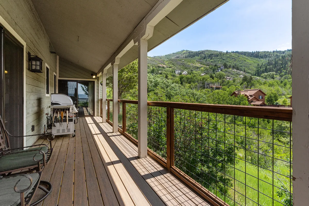This image captures the wooden wraparound deck with comfortable deck chairs, a grill, and an expansive mountain view. The scene is peaceful, with a sense of space for groups to gather for drinks, meals, or simply to soak in the scenery after a day on the slopes.