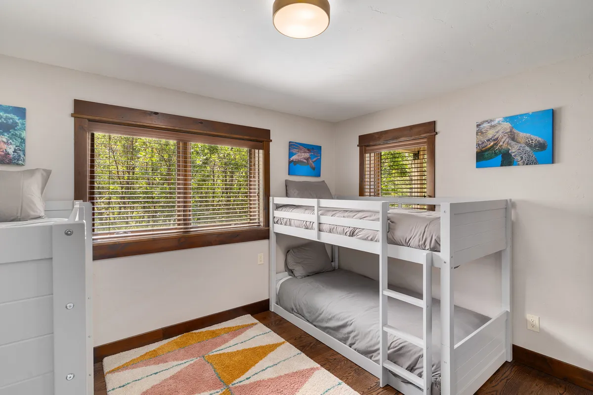 A playful interior scene featuring bunk beds with colorful bedding, a vibrant rug, and large windows offering lush green views. The room invites imaginative play and restful sleep, reinforcing the property's family-friendly layout.