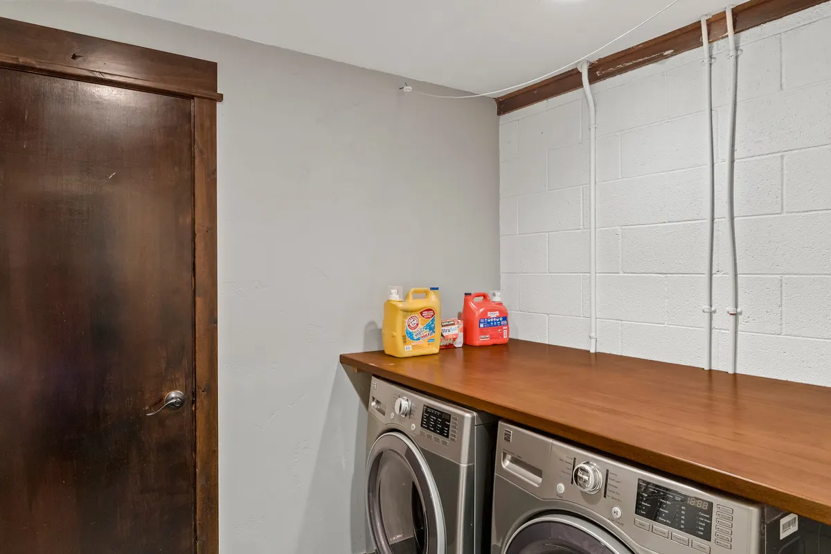 A functional and tidy laundry area with a washing machine and dryer, wooden countertop for folding clothes, and organized laundry detergents, emphasizing practical convenience for guests.