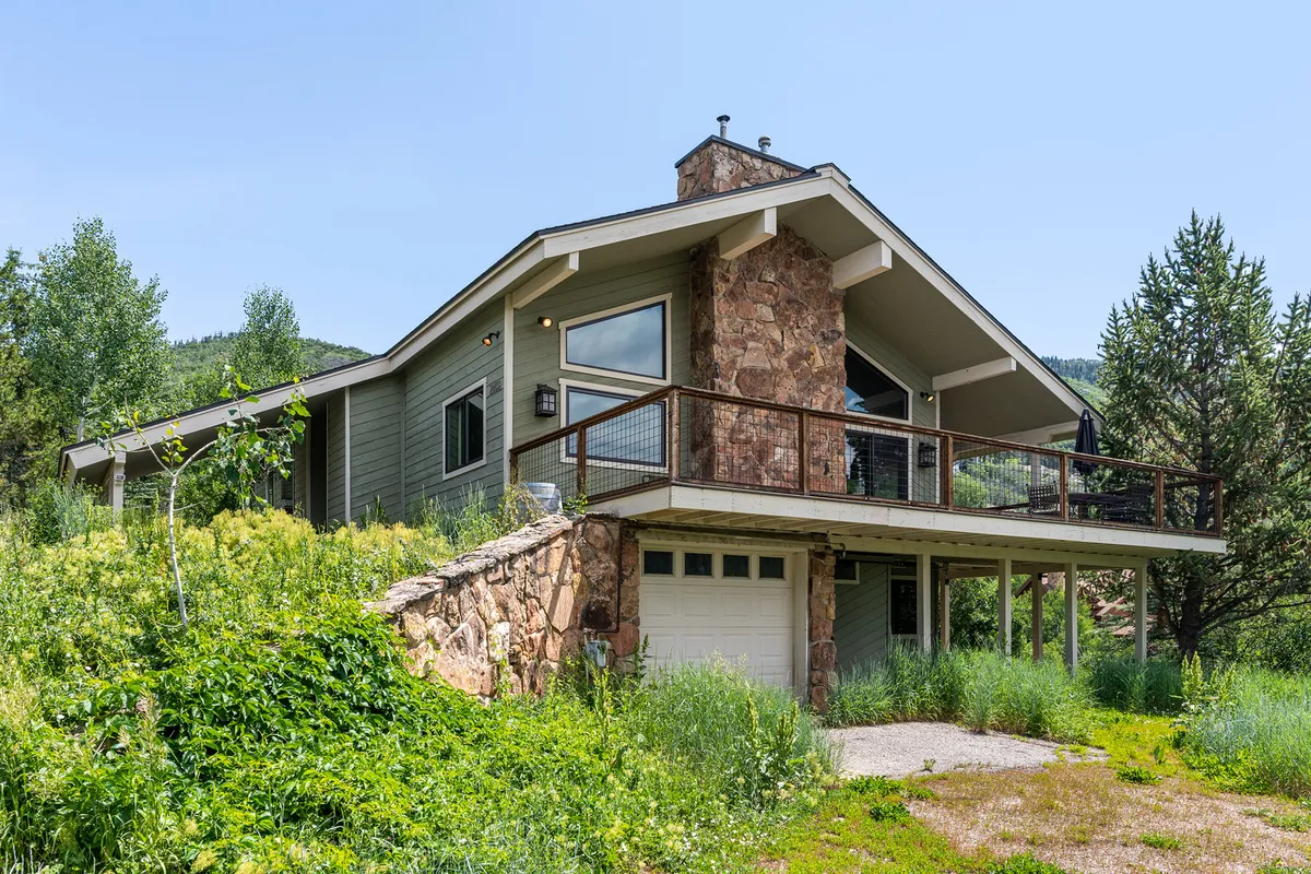 An exterior shot of the duplex's stone facade, featuring a balcony and large windows that look out onto lush greenery. The setting feels tranquil and private, hinting at the peaceful mountain ambiance highlighted in the section.