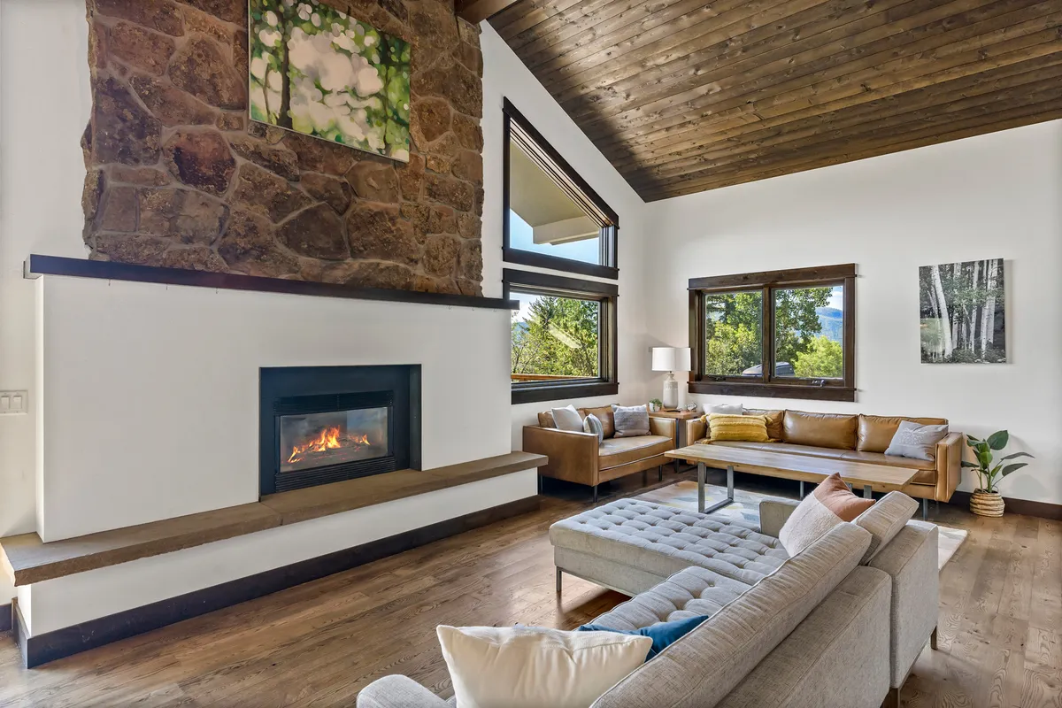 A stylish living area featuring a stone fireplace, comfortable seating arranged for intimate conversations, large windows revealing the changing light outside, and distinctive artwork. The overall ambience is warm, inviting, and perfect for relaxed evenings.