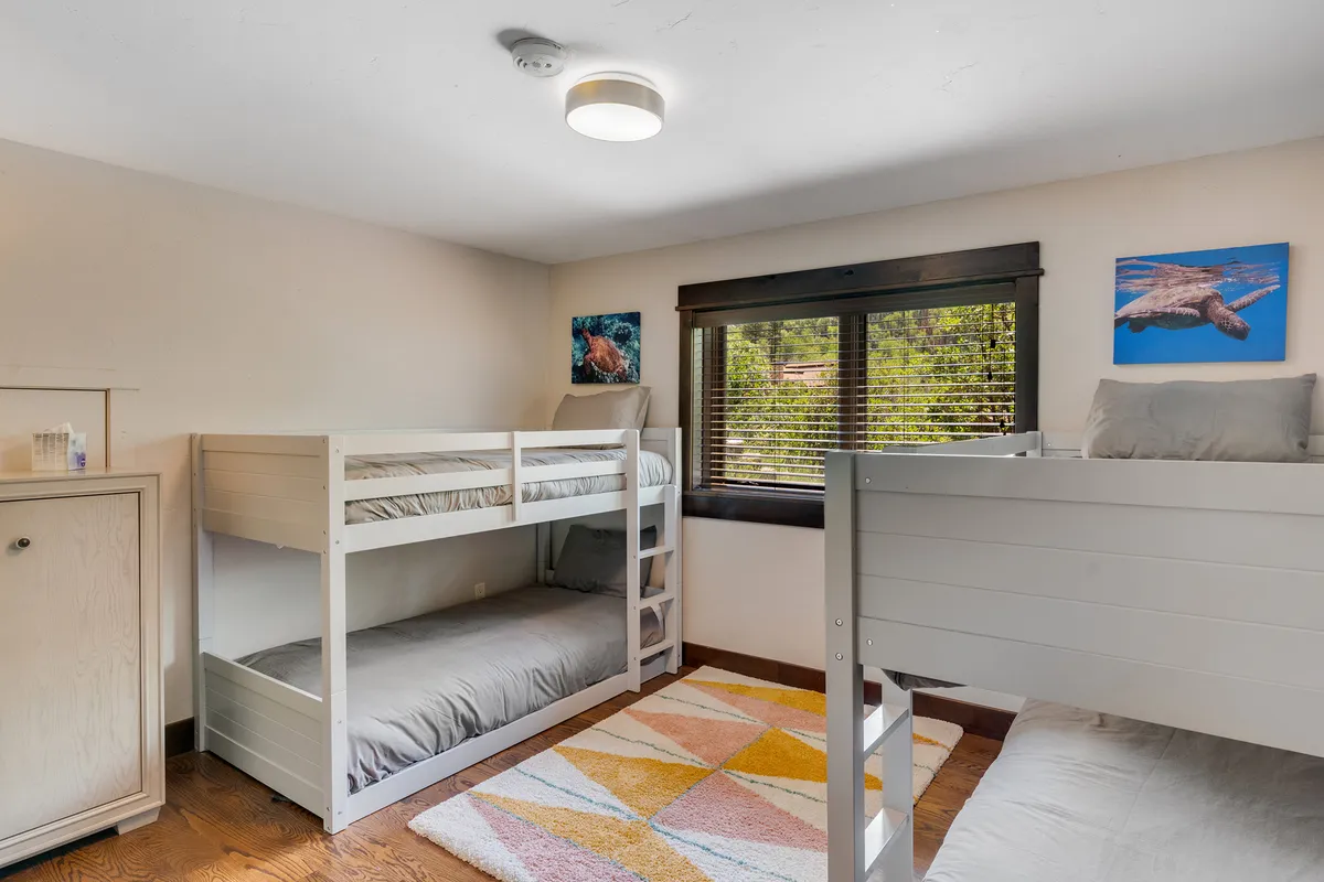 A playful bunk room with wooden bunk beds, a vibrant and colorful rug, and cheerful artwork on the walls. The space is designed for children or groups, encouraging fun and relaxation in a cozy setting.