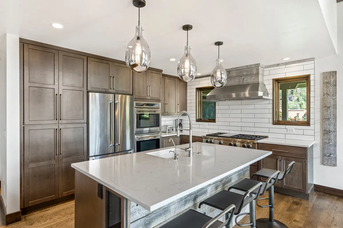 This interior shot focuses on a modern kitchen island, pendant lighting, stainless steel appliances, and wooden cabinetry. The kitchen is both functional and sociable, providing ample space for group cooking and casual conversations.