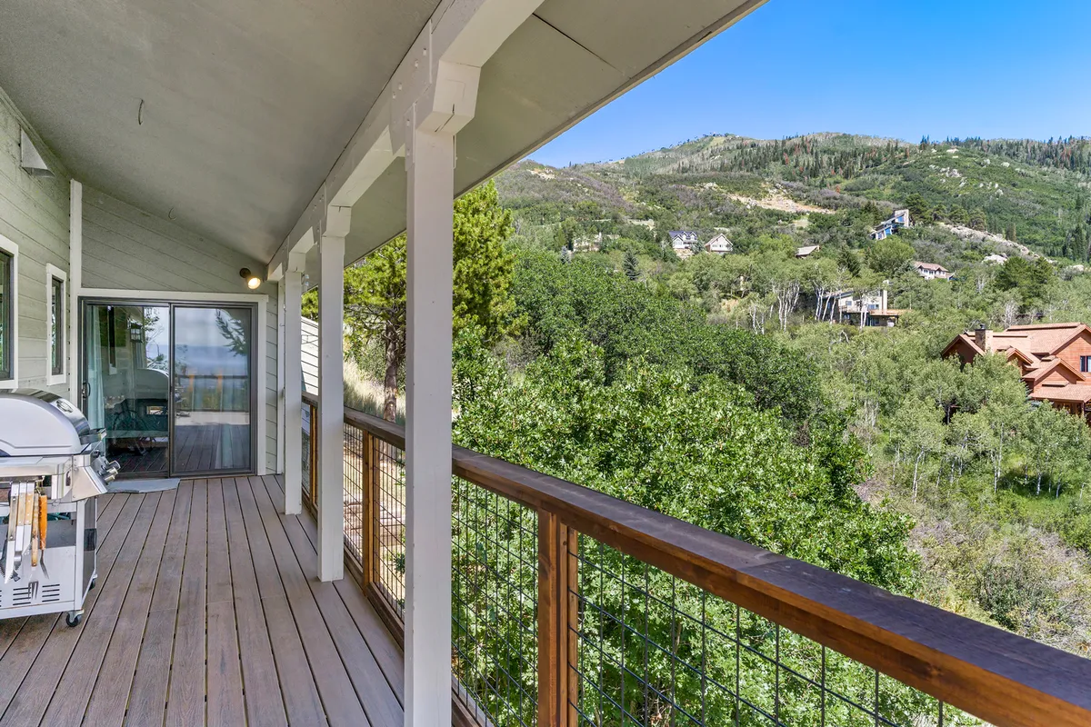 A spacious wooden deck with a grill facing majestic mountains, perfect for barbecues or unwinding in nature. The tranquil setting hints at memorable evenings watching sunsets or hosting casual cookouts with family and friends.